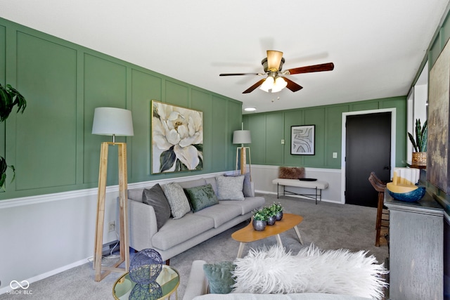 living area featuring a decorative wall, a ceiling fan, and carpet flooring