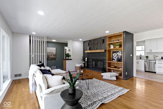 living area featuring recessed lighting, visible vents, a stone fireplace, and light wood-type flooring