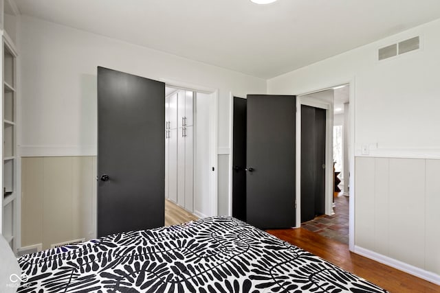 bedroom with visible vents, wood finished floors, a wainscoted wall, and a closet