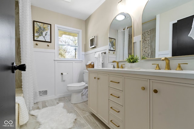 full bathroom with a sink, visible vents, toilet, a decorative wall, and wainscoting