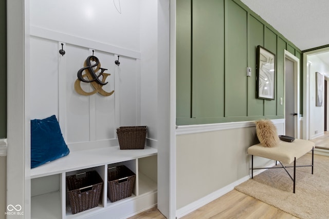 mudroom featuring light wood finished floors, a decorative wall, and baseboards