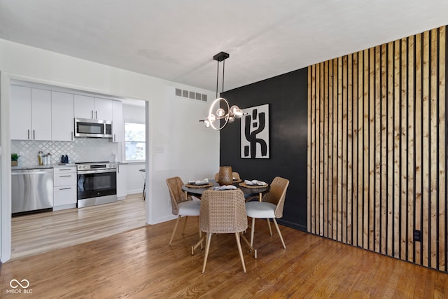 dining space with an inviting chandelier, light wood-style floors, and visible vents