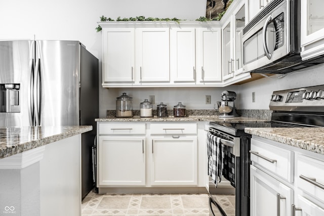 kitchen with light stone counters, glass insert cabinets, white cabinets, and stainless steel appliances