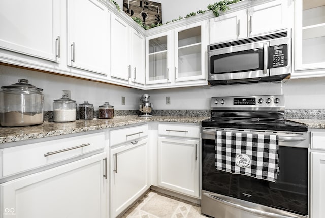 kitchen featuring glass insert cabinets, stone finish floor, white cabinets, light stone counters, and appliances with stainless steel finishes