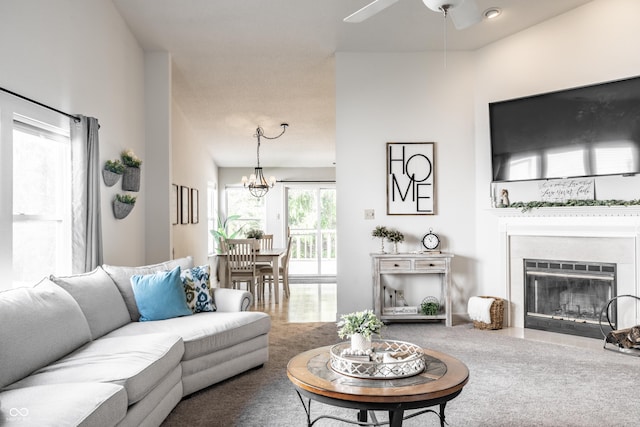 carpeted living area featuring a fireplace with flush hearth and ceiling fan with notable chandelier
