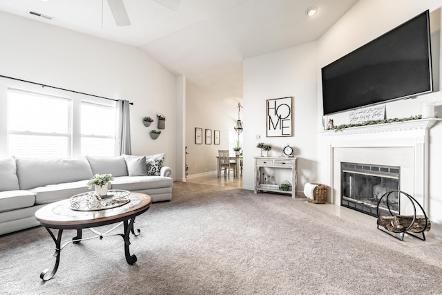carpeted living area featuring ceiling fan, visible vents, baseboards, a fireplace with flush hearth, and vaulted ceiling