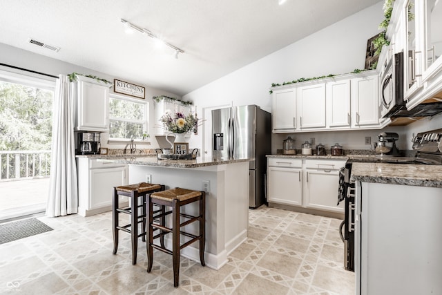 kitchen with white cabinets, a center island, stainless steel appliances, vaulted ceiling, and visible vents