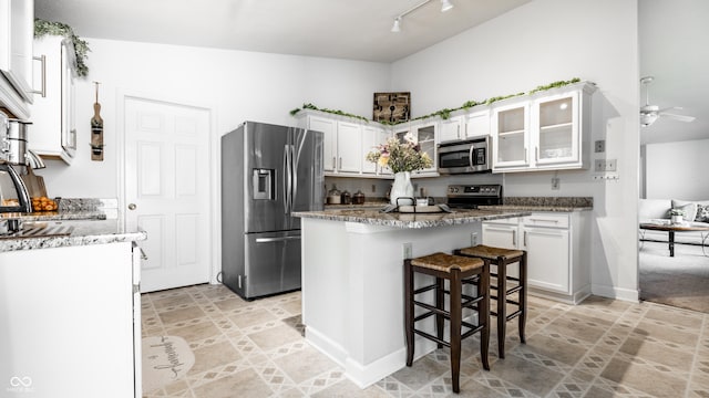kitchen with a breakfast bar area, white cabinetry, light stone counters, rail lighting, and appliances with stainless steel finishes