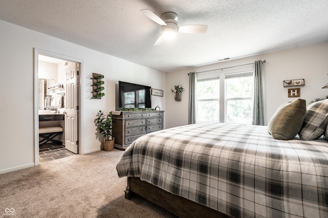 carpeted bedroom featuring a ceiling fan, a textured ceiling, visible vents, baseboards, and ensuite bath