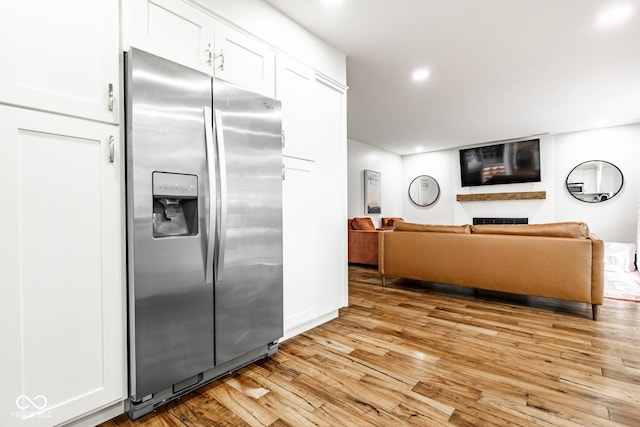 kitchen featuring stainless steel fridge, light wood finished floors, a fireplace, white cabinets, and recessed lighting