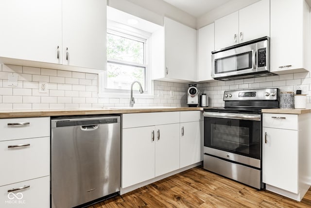 kitchen with appliances with stainless steel finishes, a sink, white cabinetry, and wood finished floors
