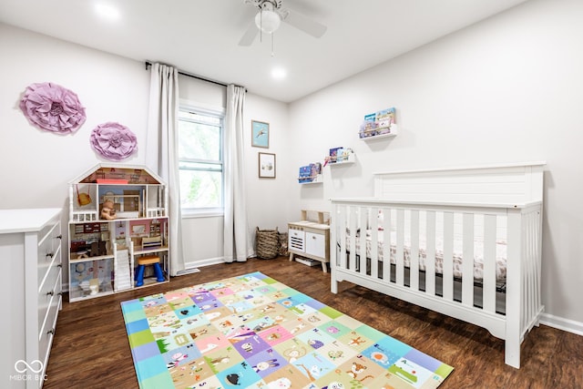 bedroom featuring wood finished floors, a nursery area, baseboards, and a ceiling fan