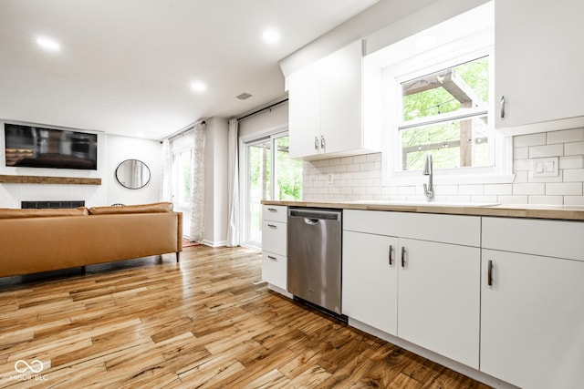 kitchen with stainless steel dishwasher, light wood-style floors, backsplash, white cabinets, and a sink