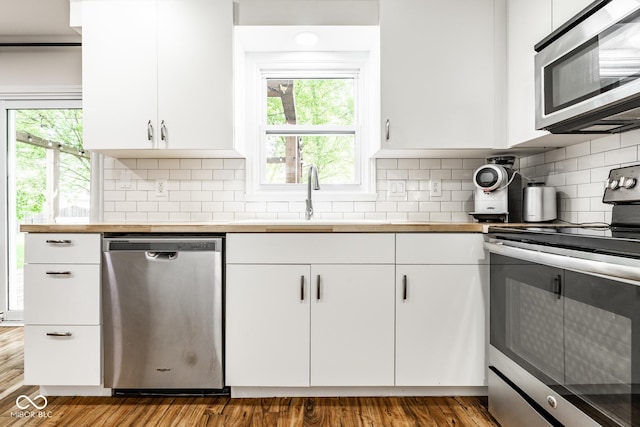 kitchen with appliances with stainless steel finishes, a sink, white cabinets, and wood finished floors