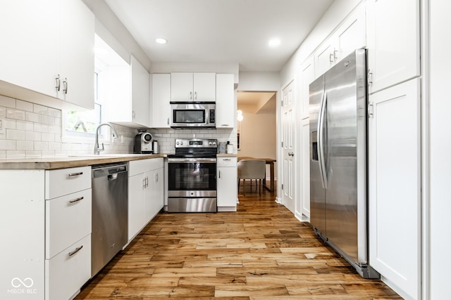 kitchen featuring stainless steel appliances, a sink, white cabinetry, tasteful backsplash, and light wood-style flooring
