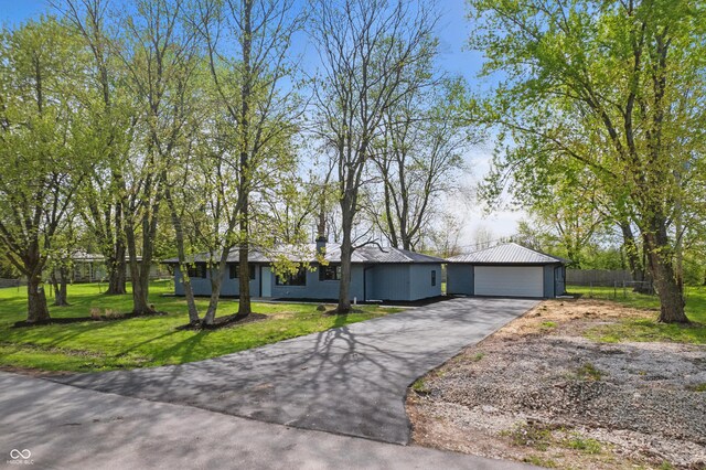 ranch-style house featuring a front yard, a garage, metal roof, driveway, and fence