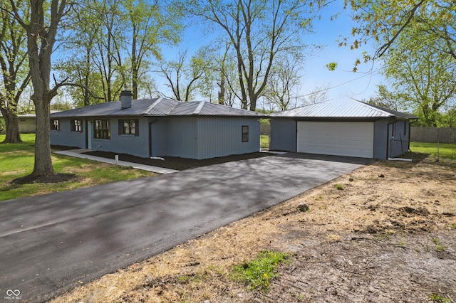 view of front of house with a garage, a chimney, metal roof, and an outbuilding