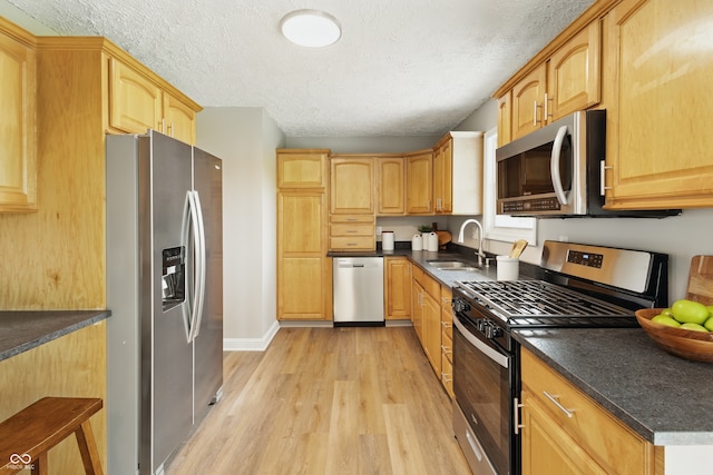 kitchen featuring a textured ceiling, light wood-style flooring, a sink, appliances with stainless steel finishes, and dark countertops