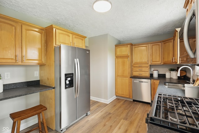kitchen with dark countertops, a sink, stainless steel appliances, and light wood-style floors