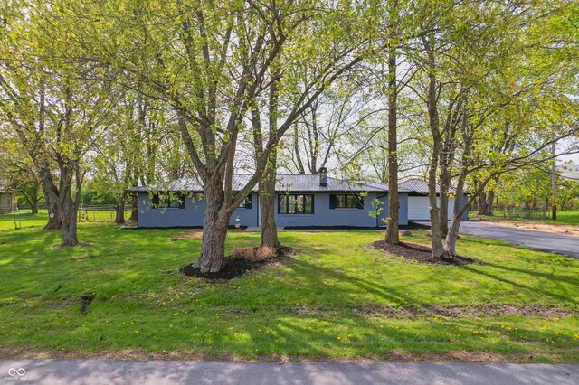 ranch-style house with a front lawn, a garage, metal roof, aphalt driveway, and fence