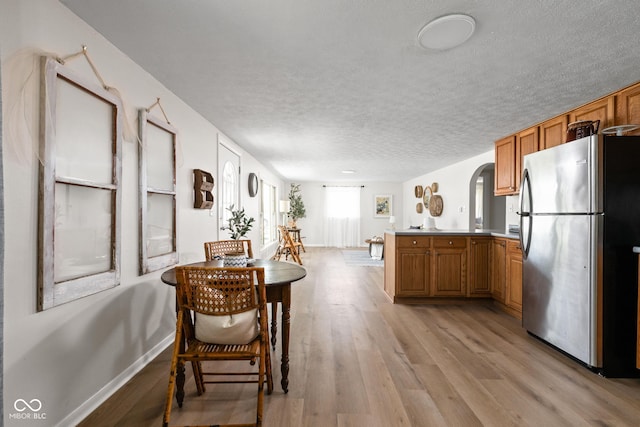 kitchen featuring freestanding refrigerator, a peninsula, light wood-style flooring, brown cabinetry, and a textured ceiling