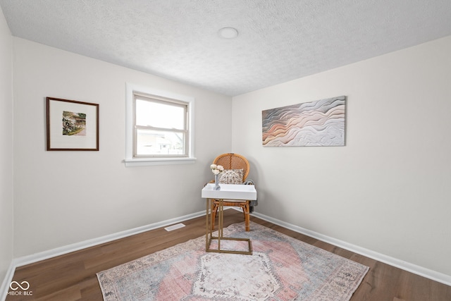 living area with wood finished floors, a textured ceiling, and baseboards