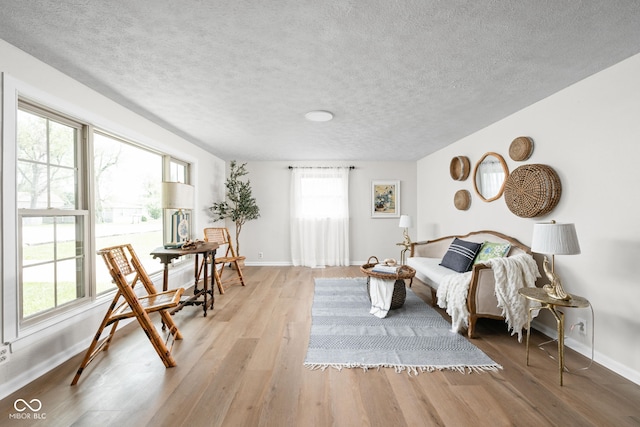 living room featuring healthy amount of natural light, light wood-type flooring, a textured ceiling, and baseboards