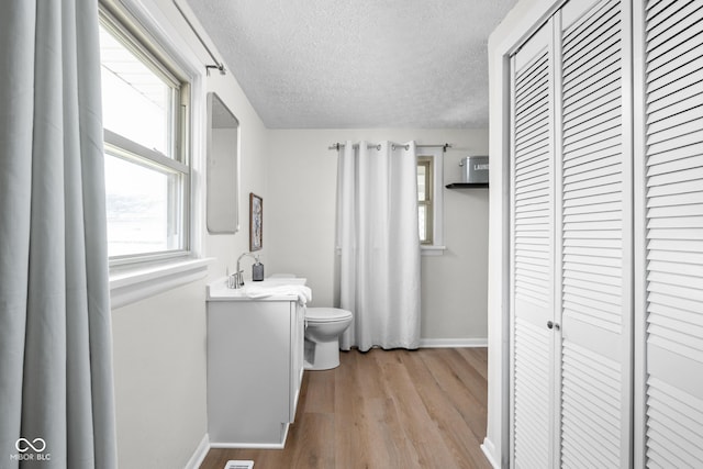 bathroom with toilet, wood finished floors, baseboards, a textured ceiling, and plenty of natural light