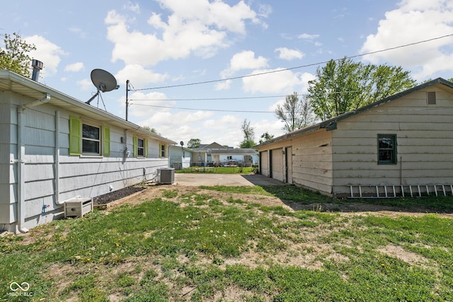 view of grassy yard with a detached garage, a patio, and central AC unit