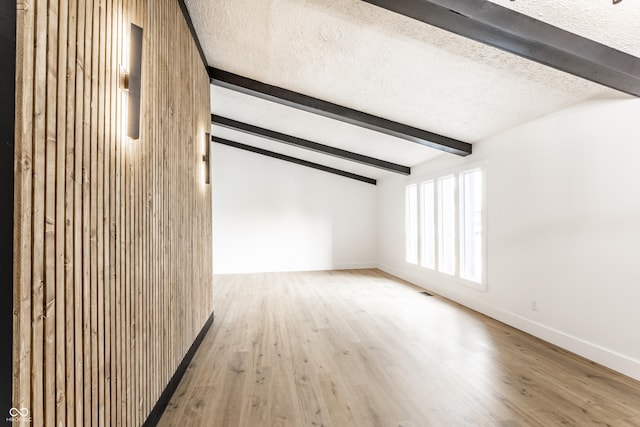 additional living space with baseboards, a textured ceiling, and wood finished floors