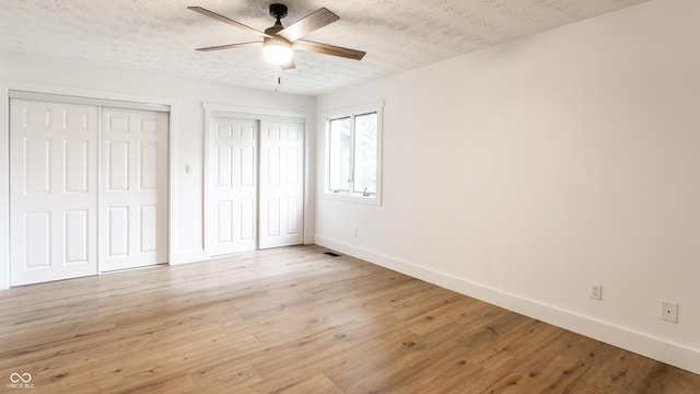 unfurnished bedroom with baseboards, a textured ceiling, multiple closets, and light wood-style floors