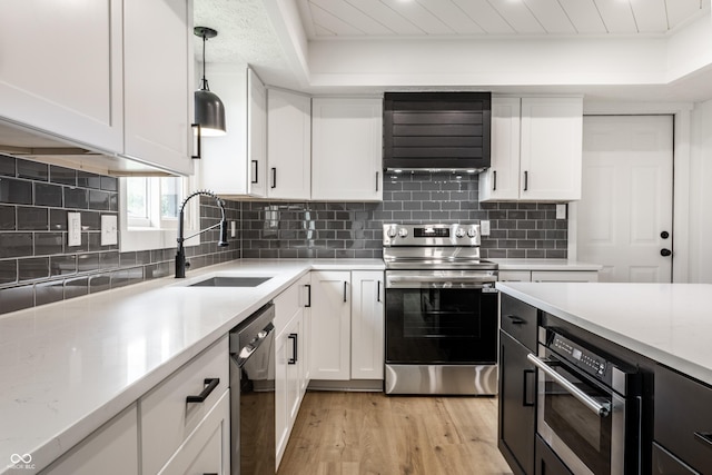 kitchen with light wood-type flooring, ventilation hood, white cabinets, a sink, and appliances with stainless steel finishes