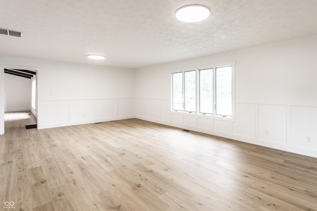 empty room with wainscoting, a decorative wall, wood finished floors, and visible vents
