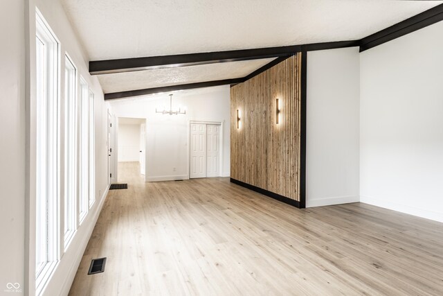 empty room with vaulted ceiling with beams, baseboards, a notable chandelier, and light wood-style floors