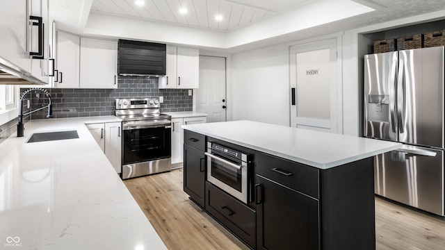 kitchen with dark cabinets, appliances with stainless steel finishes, light wood finished floors, and wall chimney exhaust hood