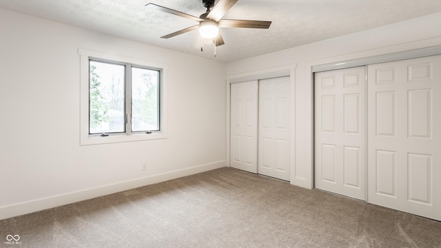 unfurnished bedroom featuring baseboards, carpet flooring, multiple closets, and a textured ceiling