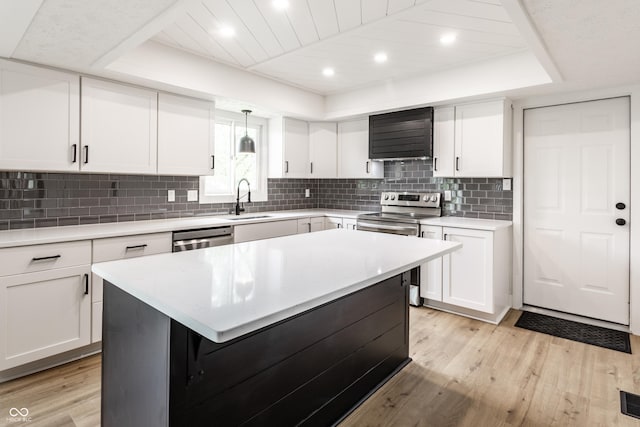 kitchen with a tray ceiling, appliances with stainless steel finishes, a sink, and light wood-style floors