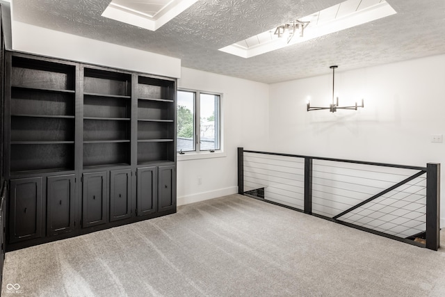 carpeted spare room with an inviting chandelier, baseboards, and a textured ceiling