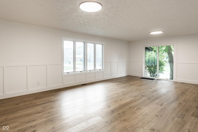 spare room featuring light wood-style floors, visible vents, and a decorative wall