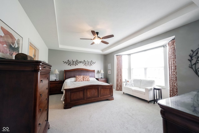 bedroom featuring light colored carpet, a tray ceiling, and ceiling fan