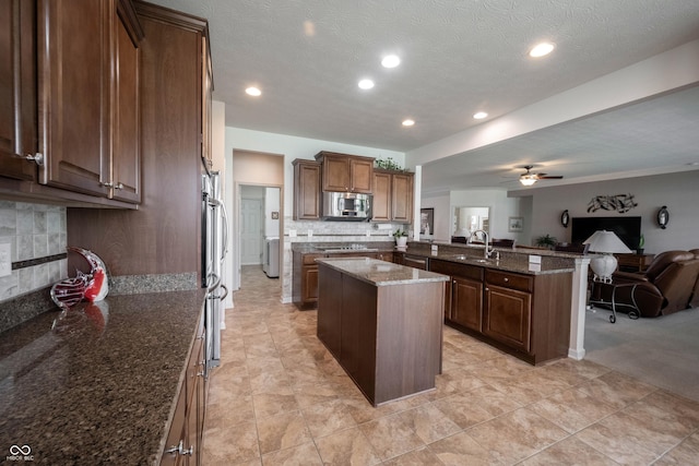 kitchen with stainless steel appliances, open floor plan, a kitchen island, decorative backsplash, and ceiling fan
