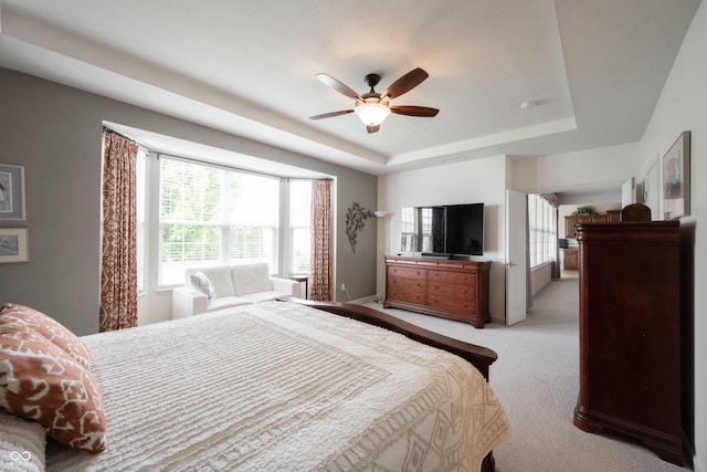 bedroom featuring a tray ceiling, light colored carpet, and ceiling fan