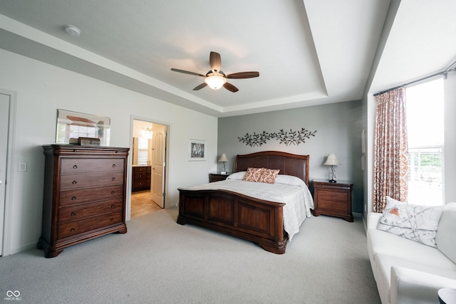 bedroom with a raised ceiling, light colored carpet, a ceiling fan, ensuite bathroom, and baseboards