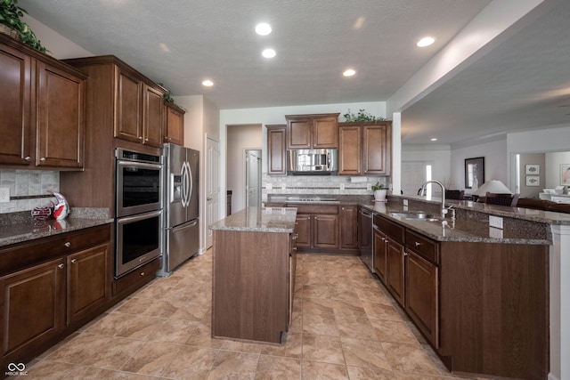 kitchen with stainless steel appliances, a sink, a peninsula, a center island, and decorative backsplash