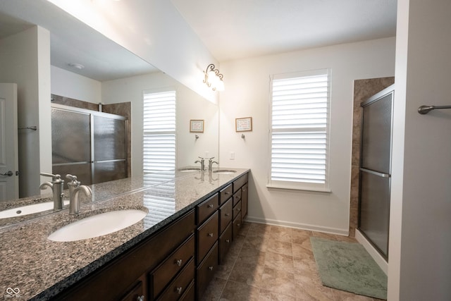 bathroom featuring a shower stall, double vanity, and baseboards