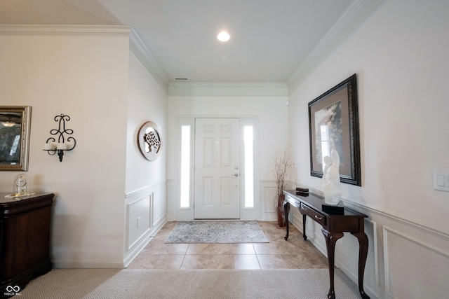 foyer entrance with crown molding, a decorative wall, light tile patterned floors, and a wainscoted wall