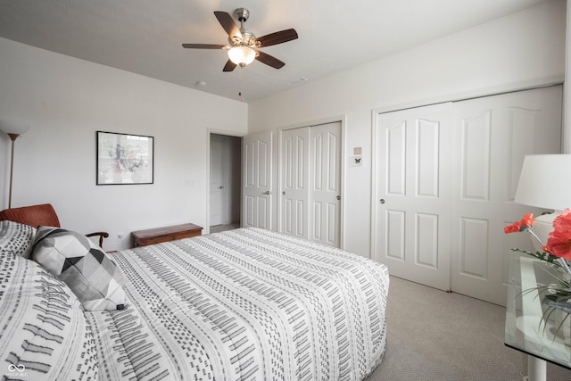 bedroom with two closets, light carpet, and ceiling fan