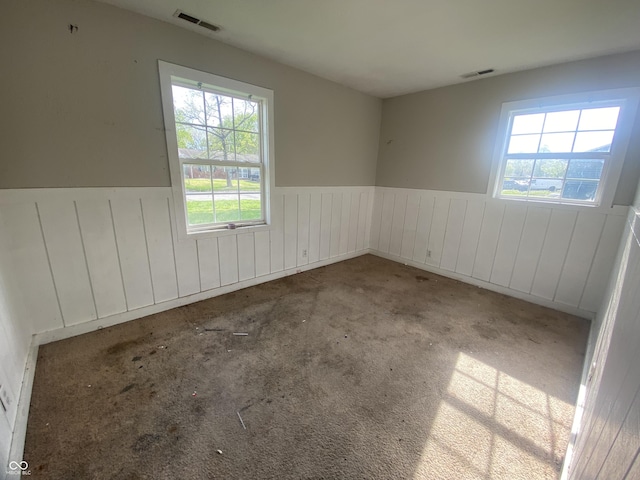 spare room with visible vents, a healthy amount of sunlight, and a wainscoted wall