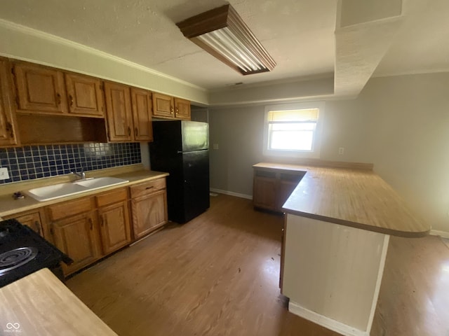 kitchen with light countertops, black appliances, a sink, light wood-type flooring, and a peninsula