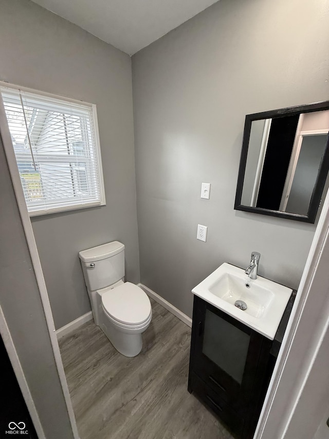 half bathroom featuring toilet, vanity, wood finished floors, and baseboards
